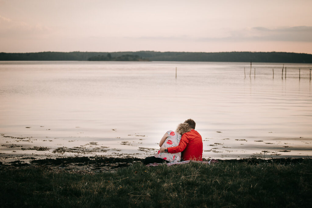 Parfotografering ved stranden – par sidder og ser ud over vandet.