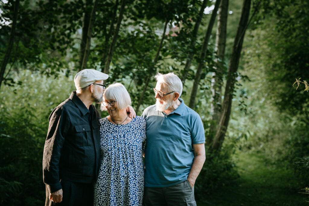 Mand med sin mor og far, stående tæt sammen med varme smil i en smuk, naturlig baggrund, der fanger familiens kærlighed og samhørighed.