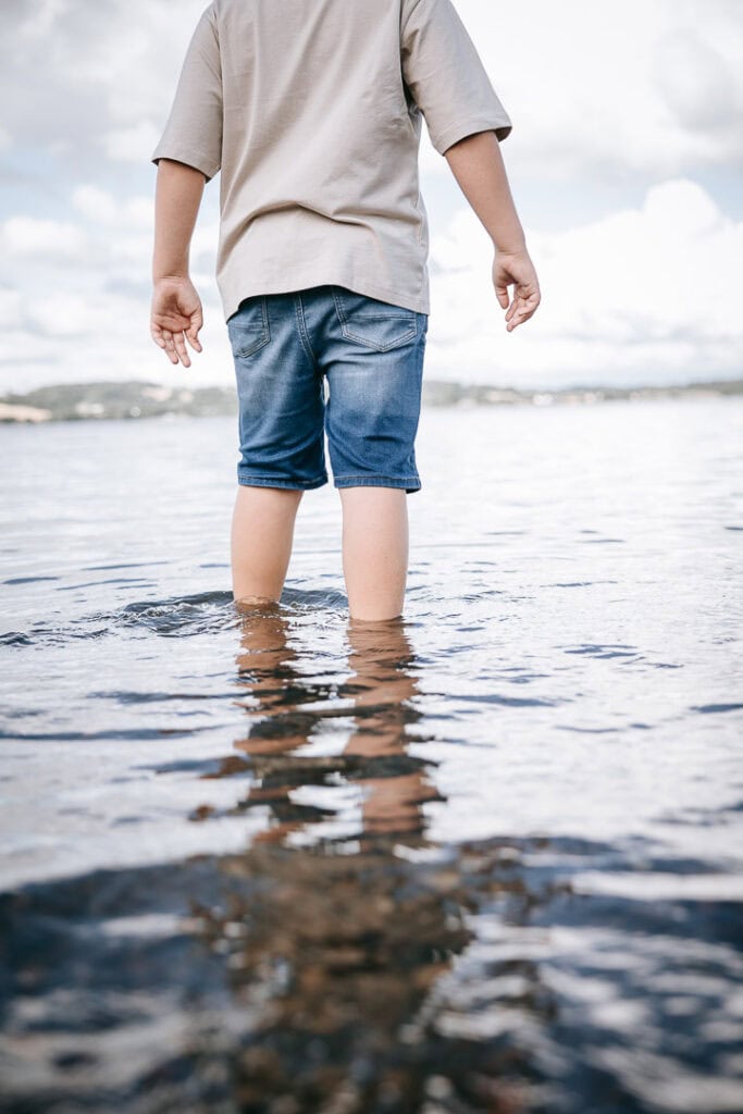Barn står i vandkanten med bare ben – naturlig børnefotografering ved stranden i Lemvig.