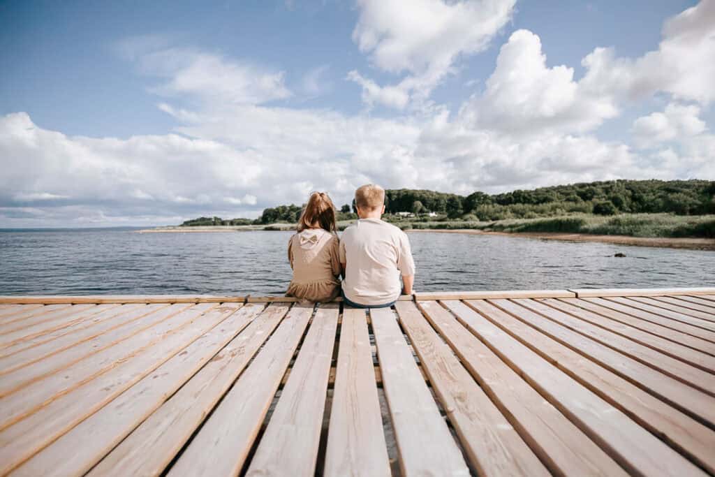 To børn sidder sammen på badebro med udsigt over fjorden – familiefotograf Nordvestjylland.