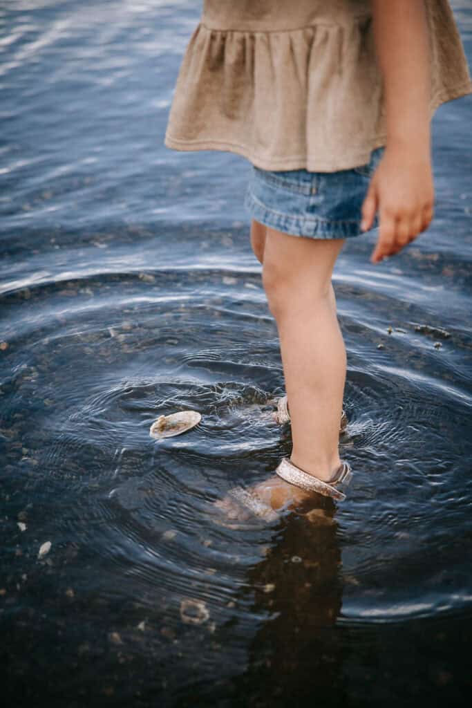 Barn står med fødderne i vandet og leger med musling – naturligt familiefoto i Holstebro.