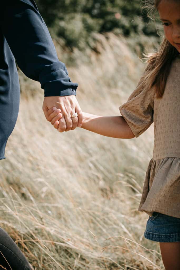 Forælder og barn holder hinanden i hånden på eng ved Struer Fjord.