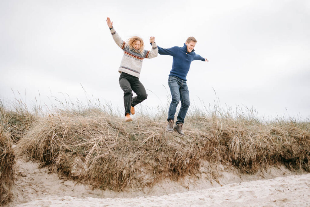 Legende par hopper i klitterne under fotosession ved Vesterhavet.