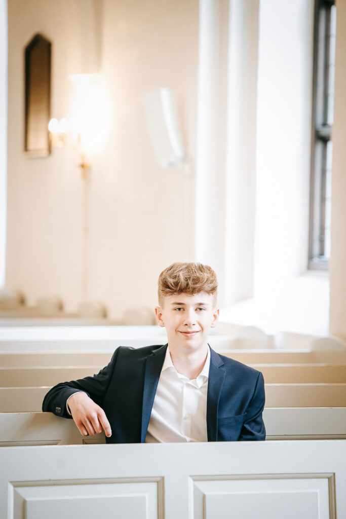 Konfirmant fotograferet i kirken. han kigger ind i kameraet
