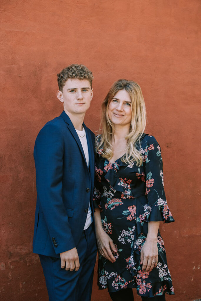 Konfirmand står sammen med sin mor foran rustfarvet baggrund og ser roligt ind i kameraet.