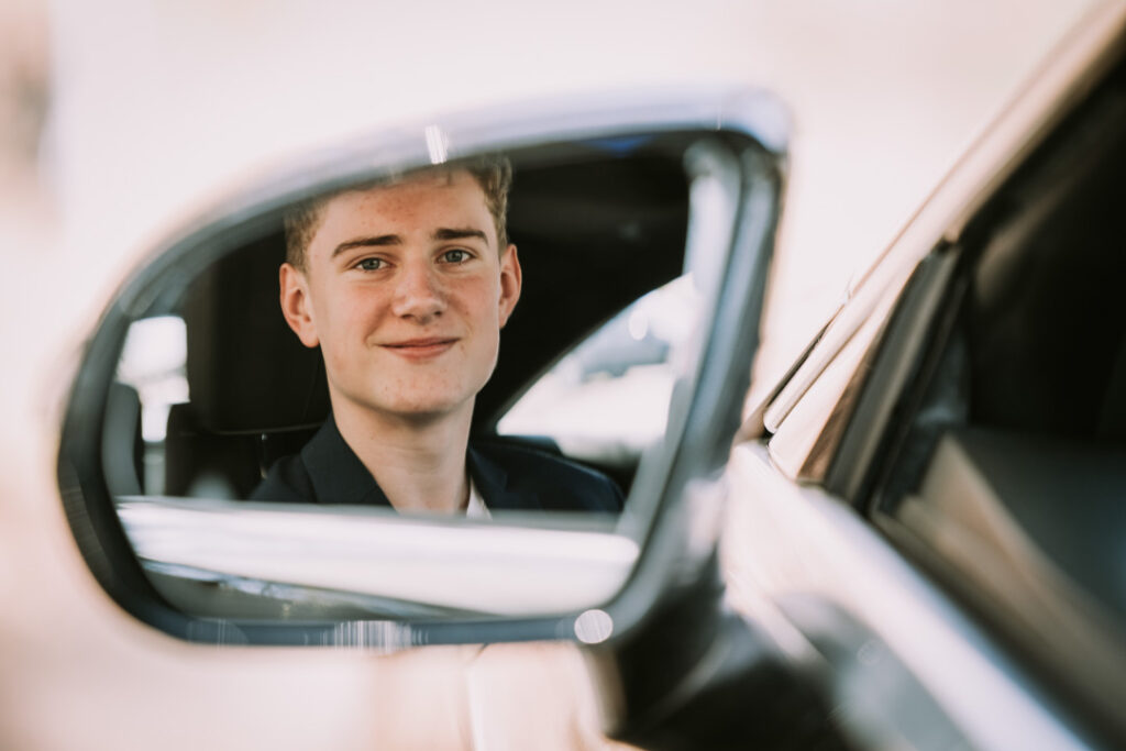 Portræt af konfirmand i bil set gennem sidespejlet med rolig stemning og naturligt lys.