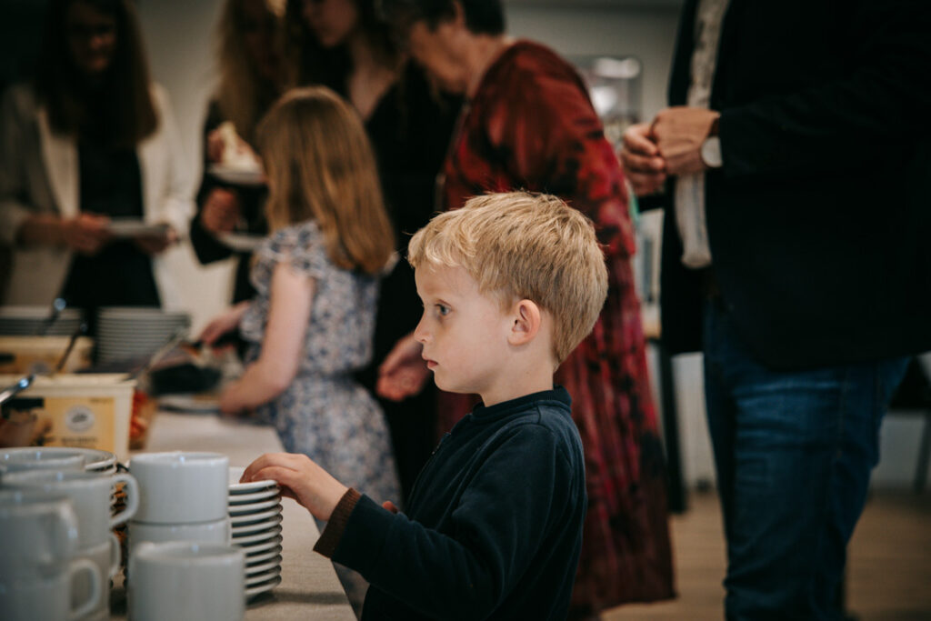 Stemningsbillede fra konfirmationsfest med gæster og barn i fokus i et ægte øjeblik.