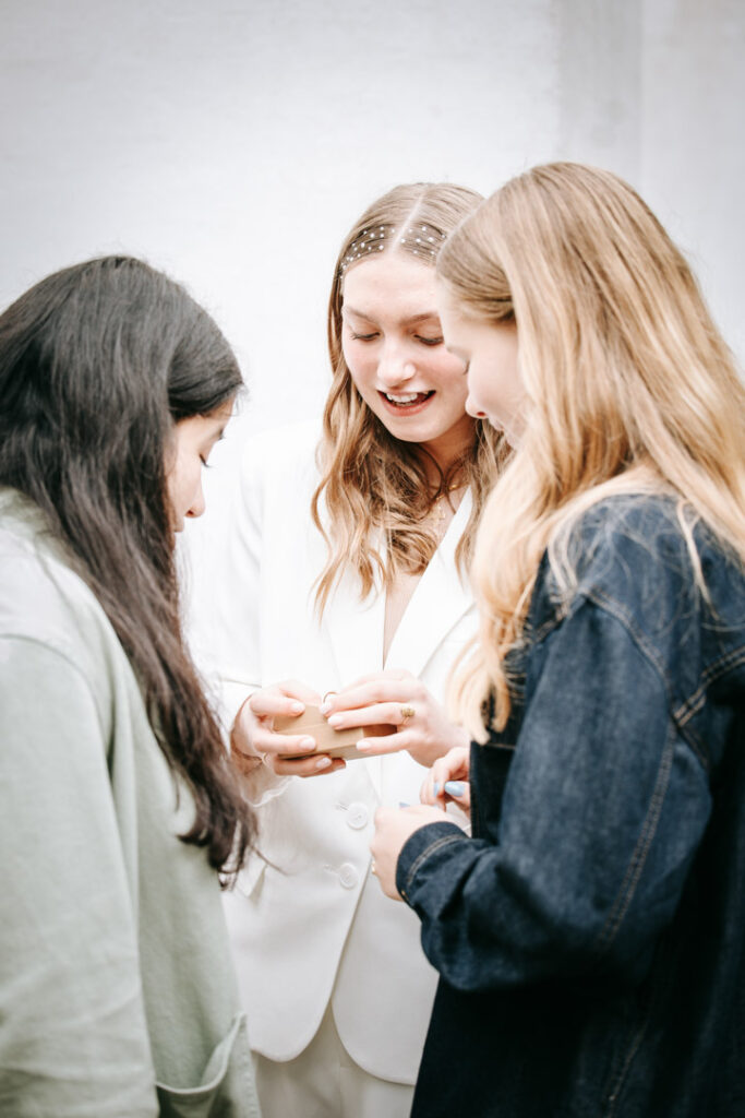 Konfirmand står sammen med veninder og ser på en gave efter konfirmationen, fanget i et naturligt øjeblik.